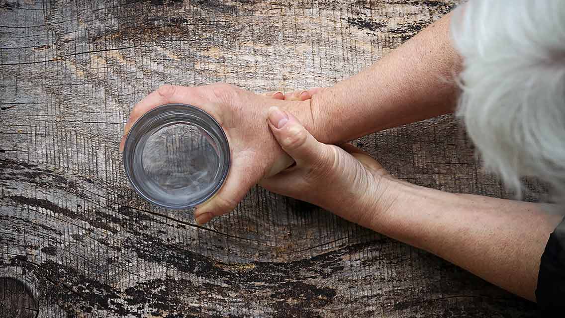 a woman holds her wrist while she picks up a glass of water