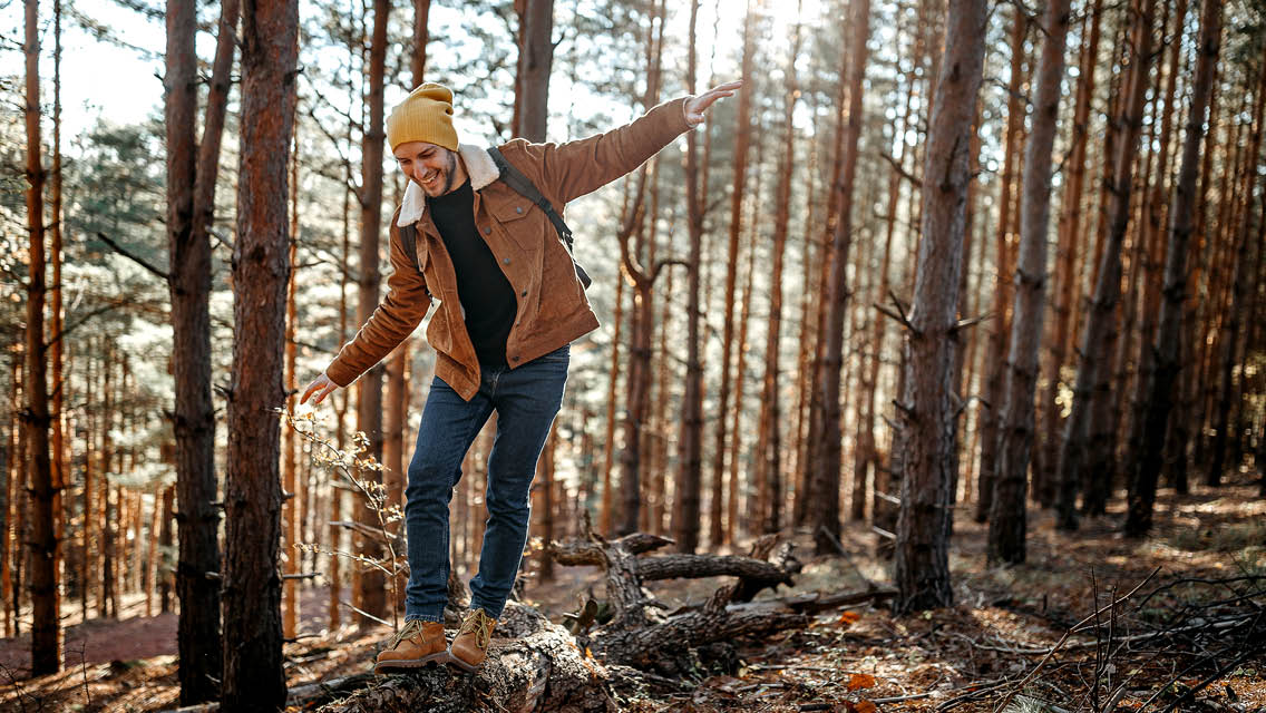 a man balances while walking over a downed tree trunk