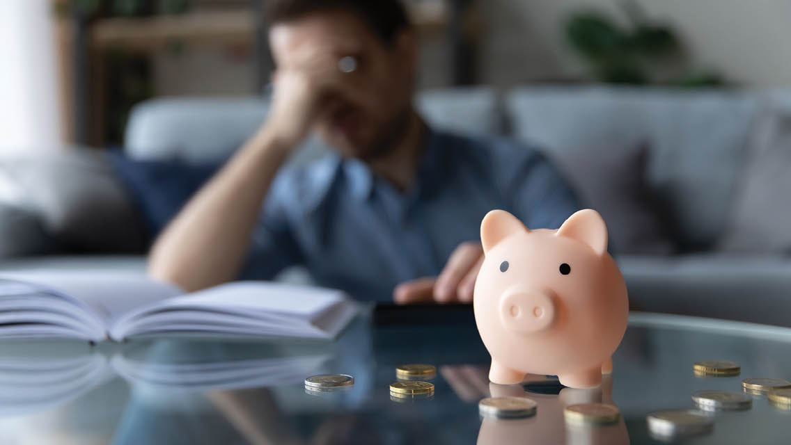 a man holds his head in frustration with a piggy bank and coins