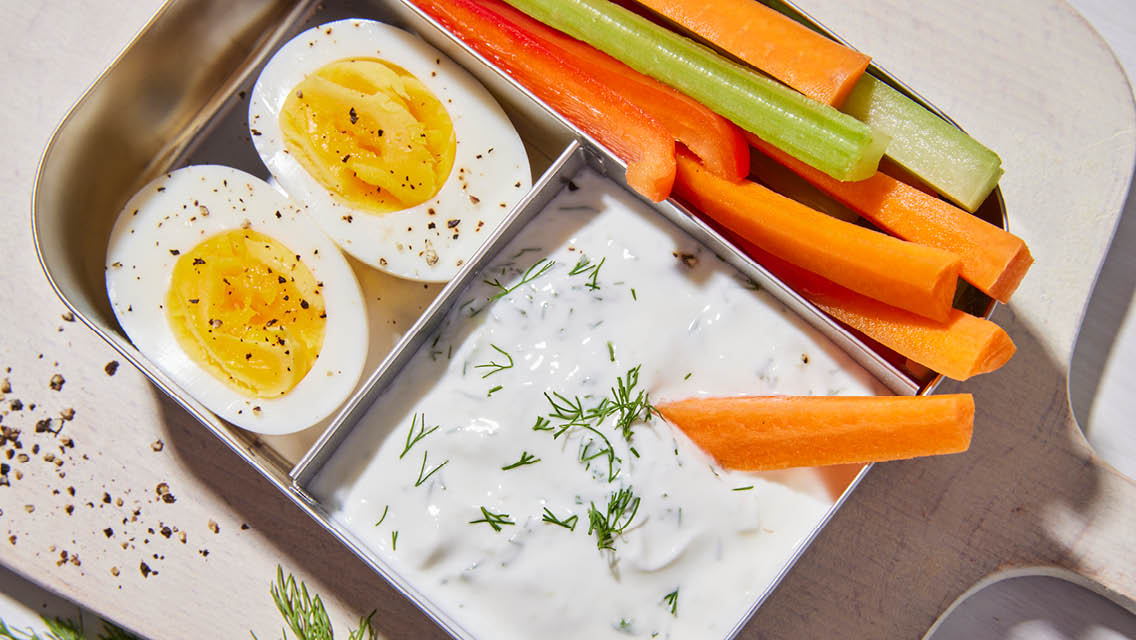 a bento box with tzatziki dressing, boiled egg and veggie sticks