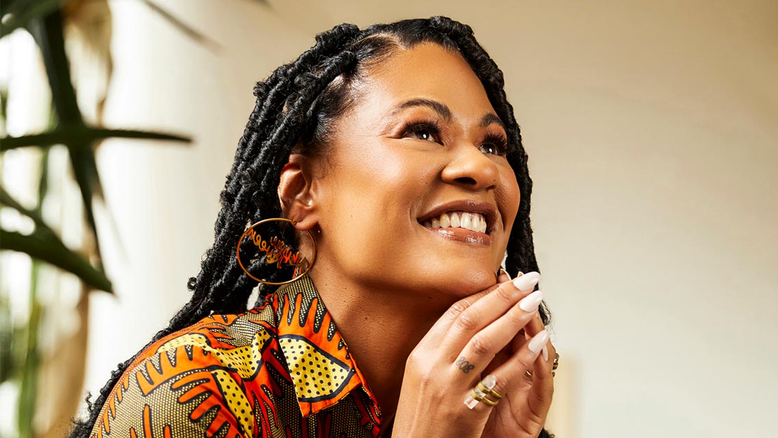 A women smiles with her hands clasped under her chin.