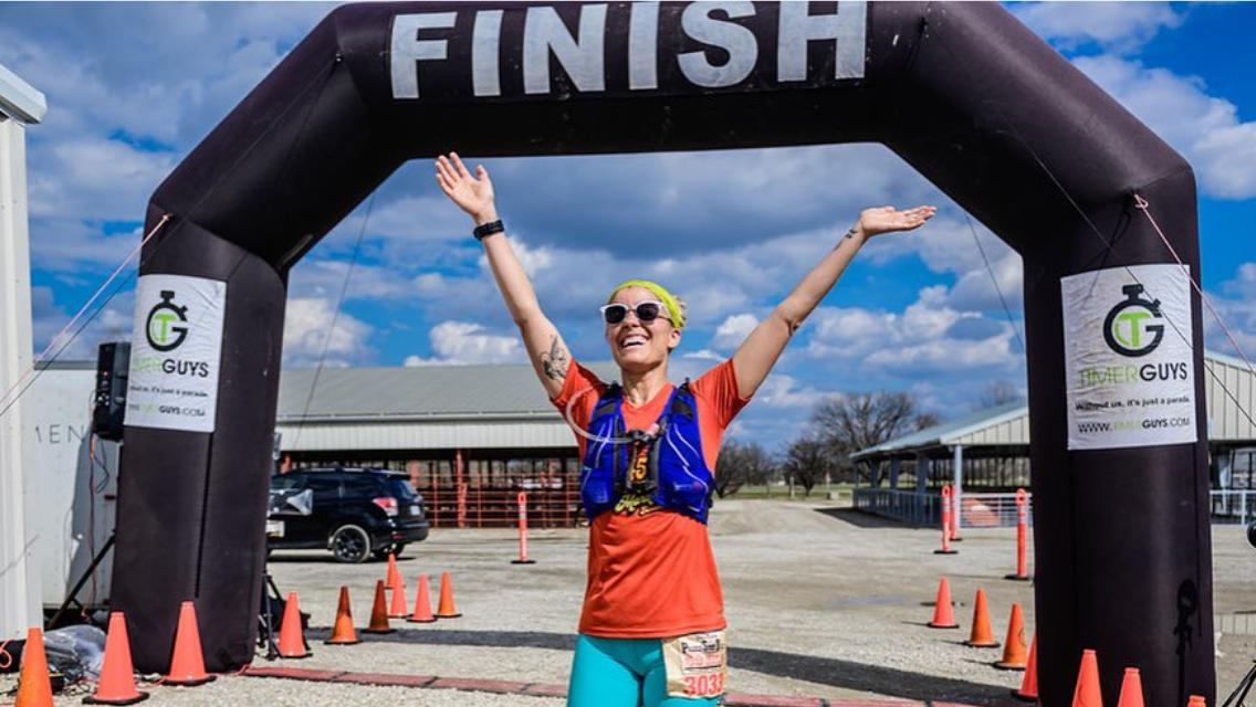 Barbara Powell beneath a finish line of a running race.