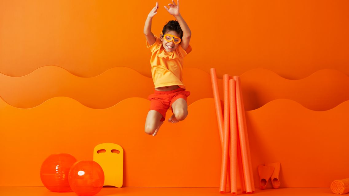 A young child jumping into the air with swimming gear on.