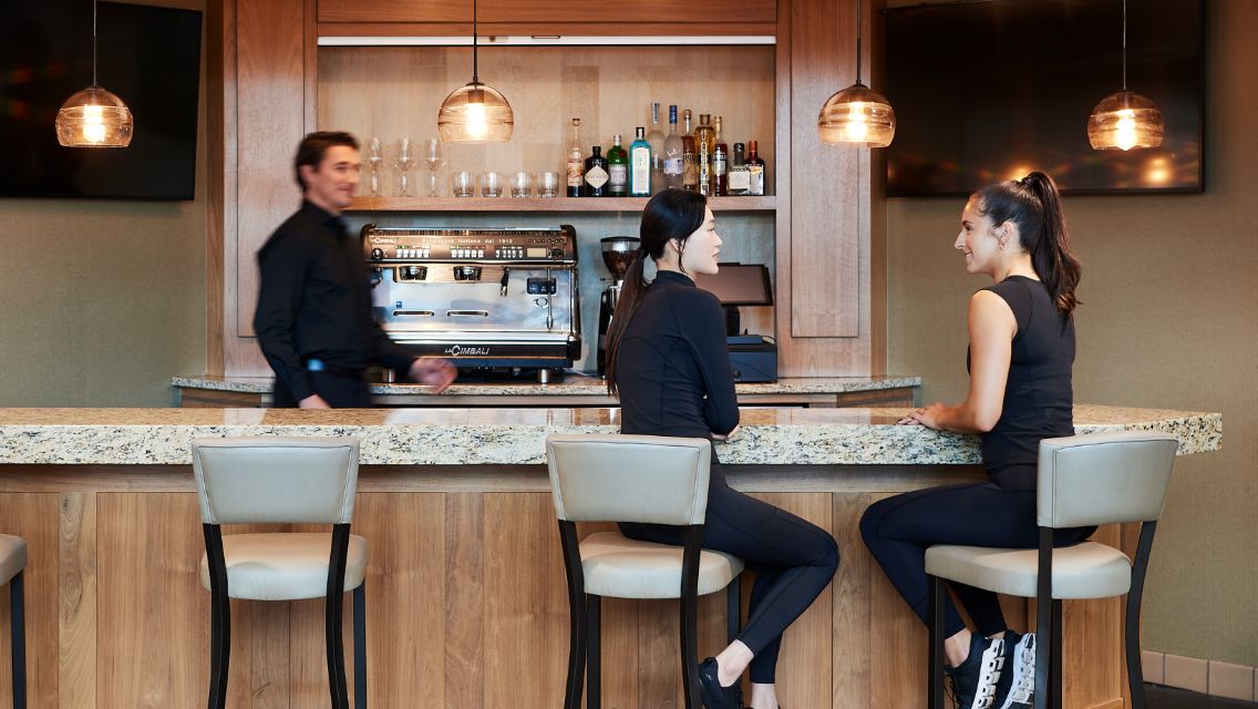 A couple of women sitting at a bar that serves coffee and alcohol.