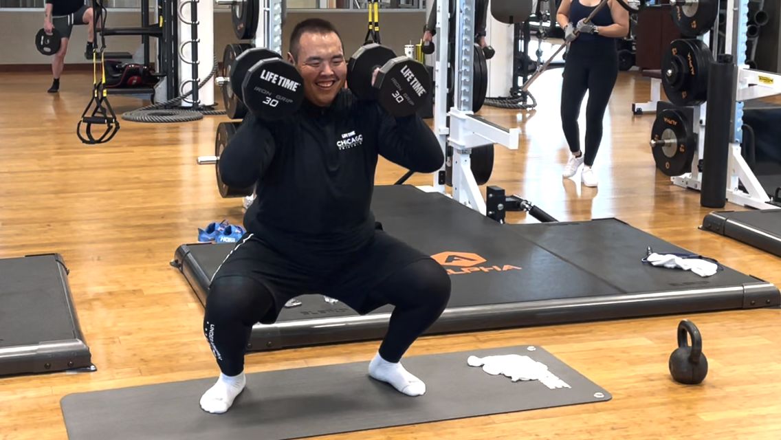 Bayar Bayarsaikhan doing a squat with dumbbells in a Life Time club.