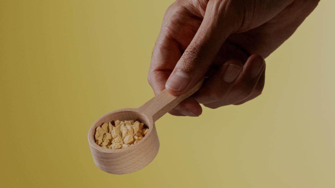 A hand holding a scoop of protein powder.