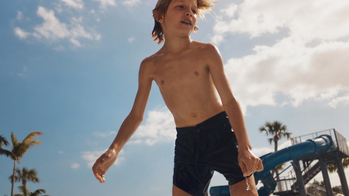 A young boy in front of a water slide outside at a Life Time pool.