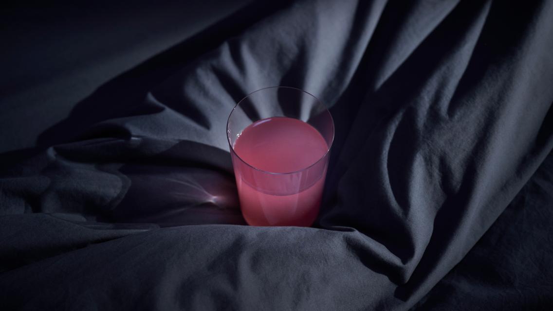 A glass with LTH Dream resting on sheets on a bed.