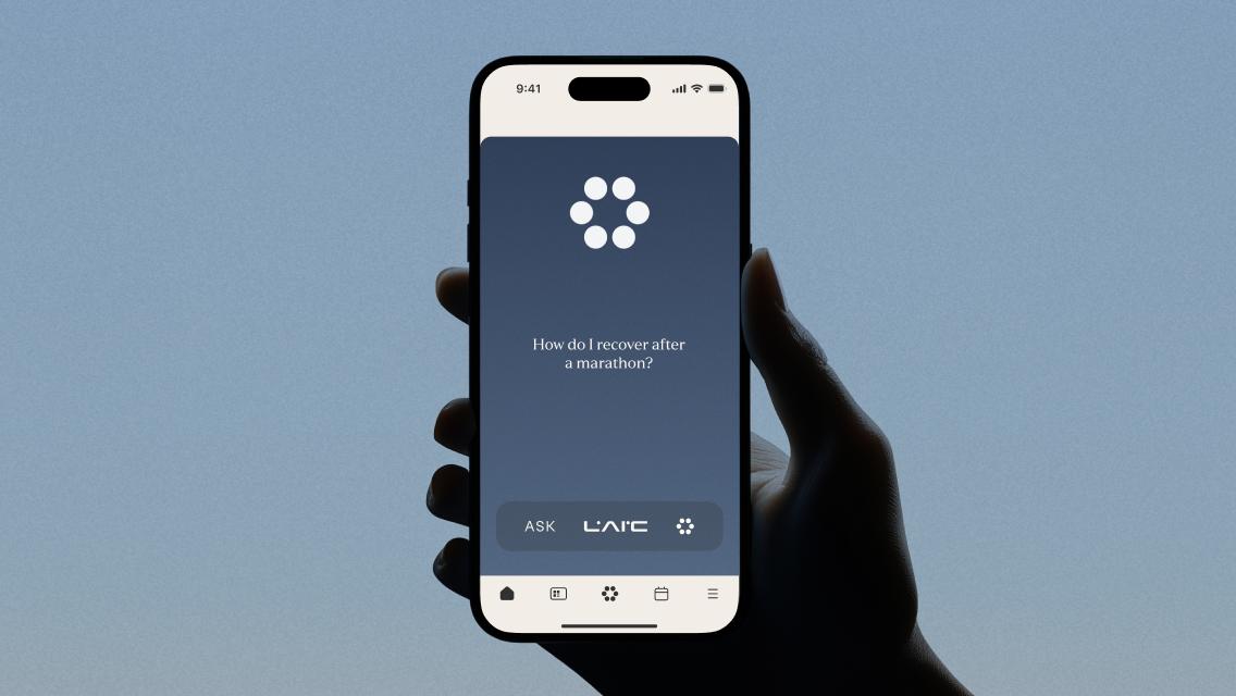 A hand holding a phone with LAIC open in the Life Time app, showing a question that says, "How do I recover after a marathon?"