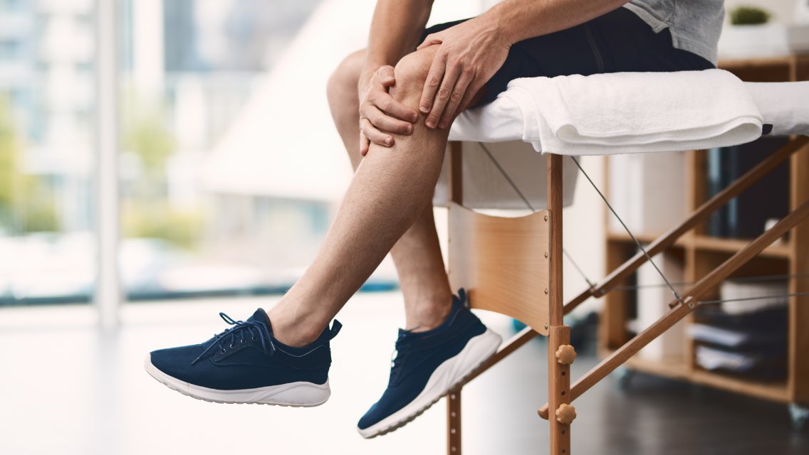 A person in workout gear sitting while grasping their knee in pain.