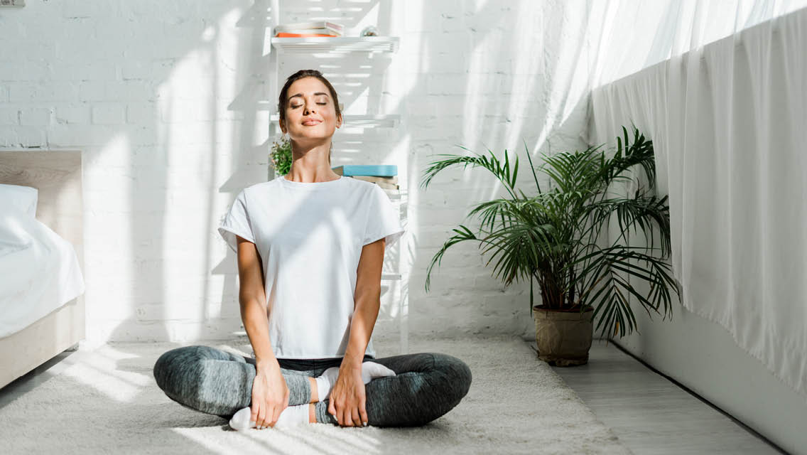 a woman sits cross legged, meditating, in her bedroom