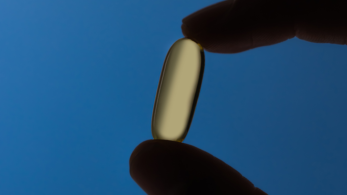 Two fingers holding a capsule of LTH Glow Omega-3 Fish Oil in them.