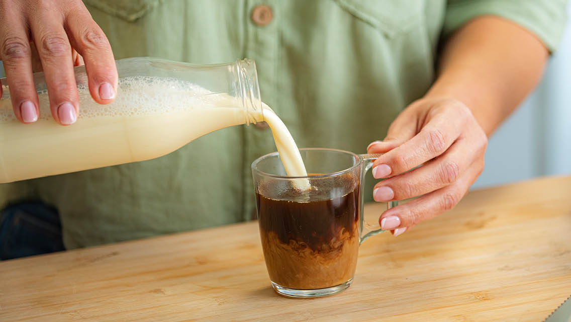 a person pours almond milk into their coffee