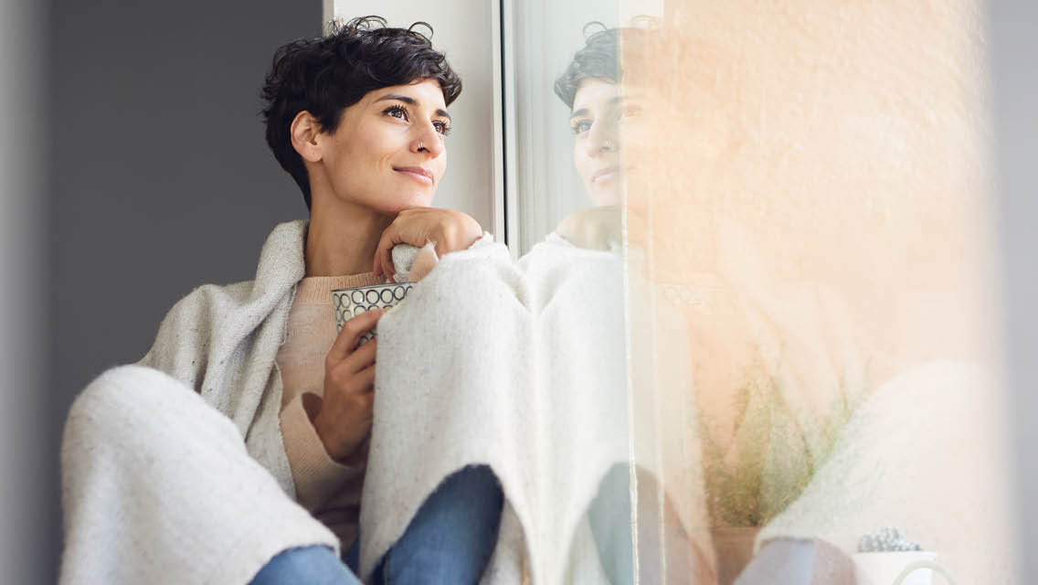 a woman wrapped in a blanked looks out a window