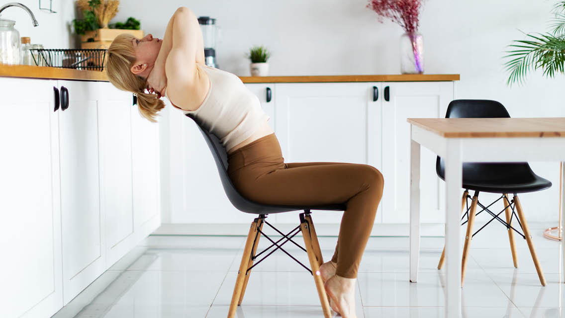 a woman holds a seated backbend in her chair