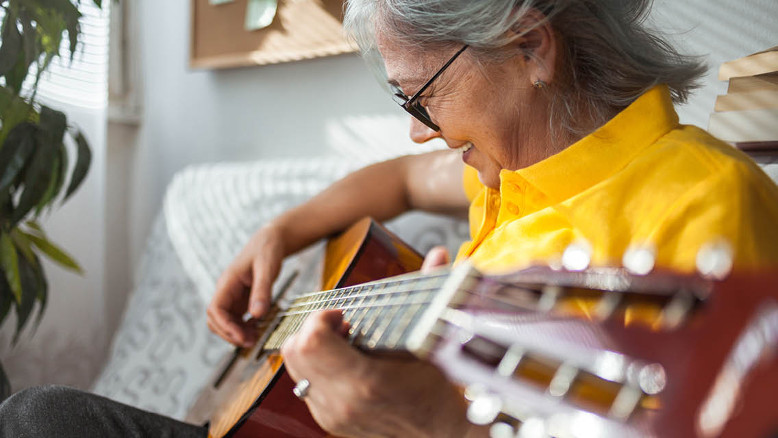 a senior aged woman plays the guitar