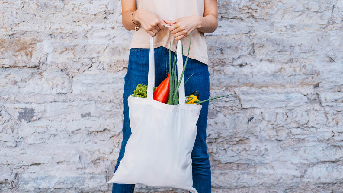 a person stands with a cloth bag filled with groceries