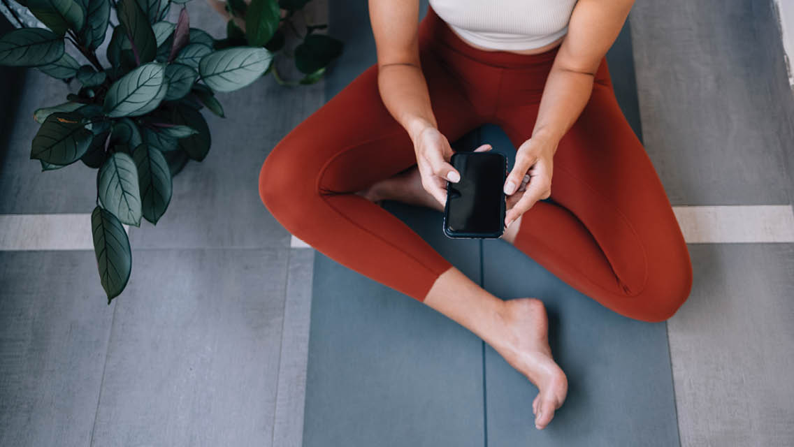 a person sits on a yoga mat holding a phone
