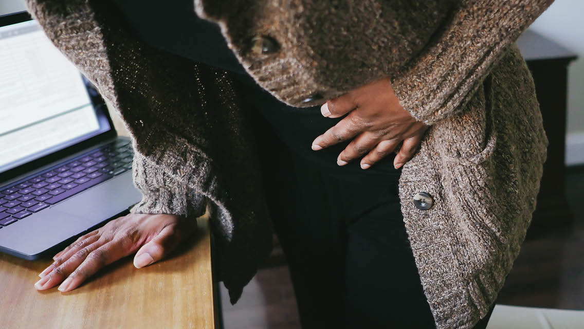a woman hunches over her desk with her hand on her stomach