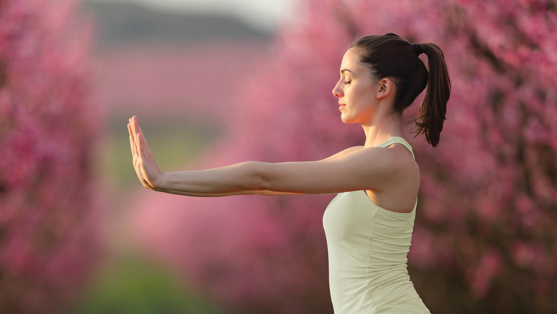 a woman practices tai chi with cherry blossoms in the background