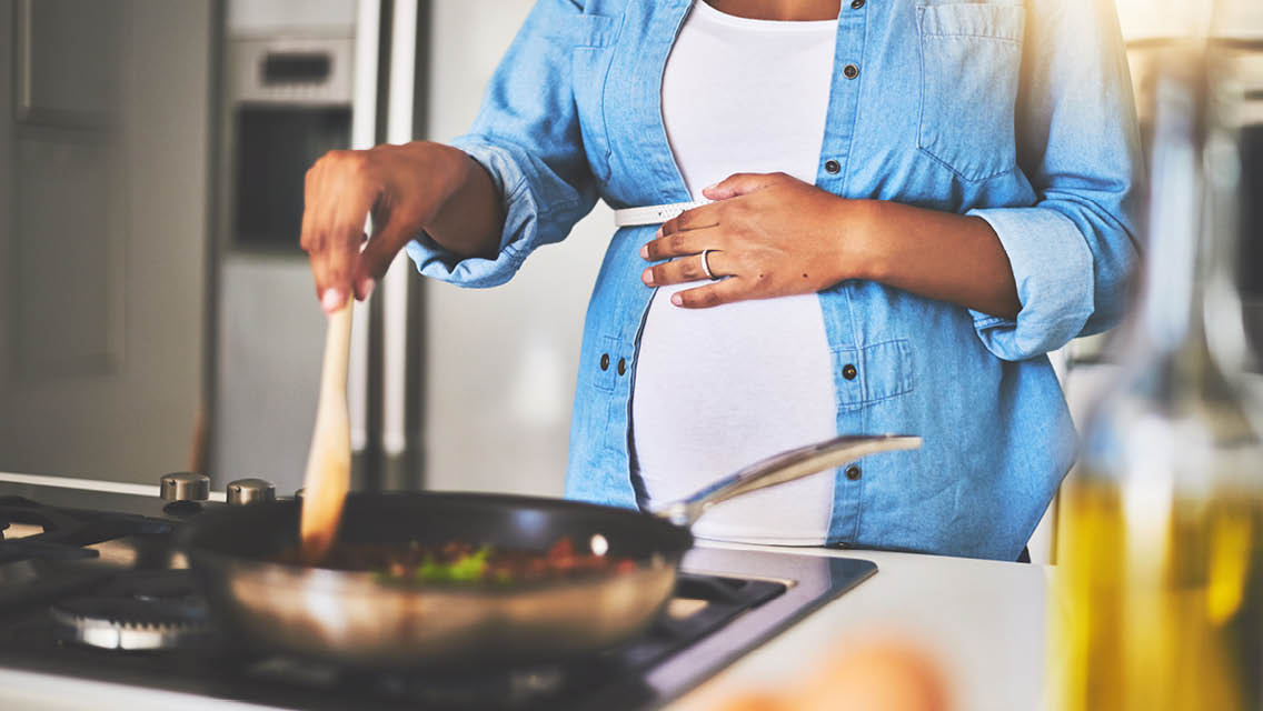 a pregnant woman cooking dinner