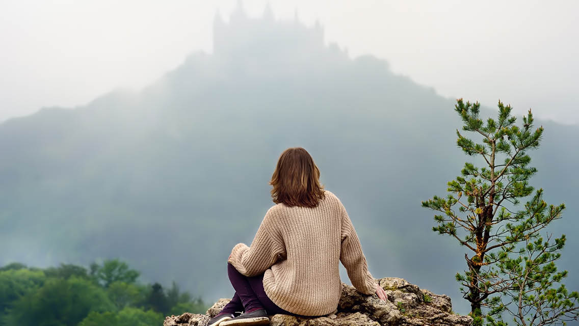 a woman looks at a castle on top of mountain.