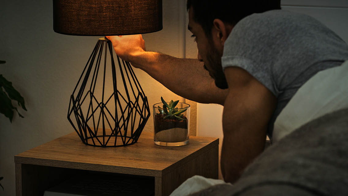 a man turns a light off while in bed.