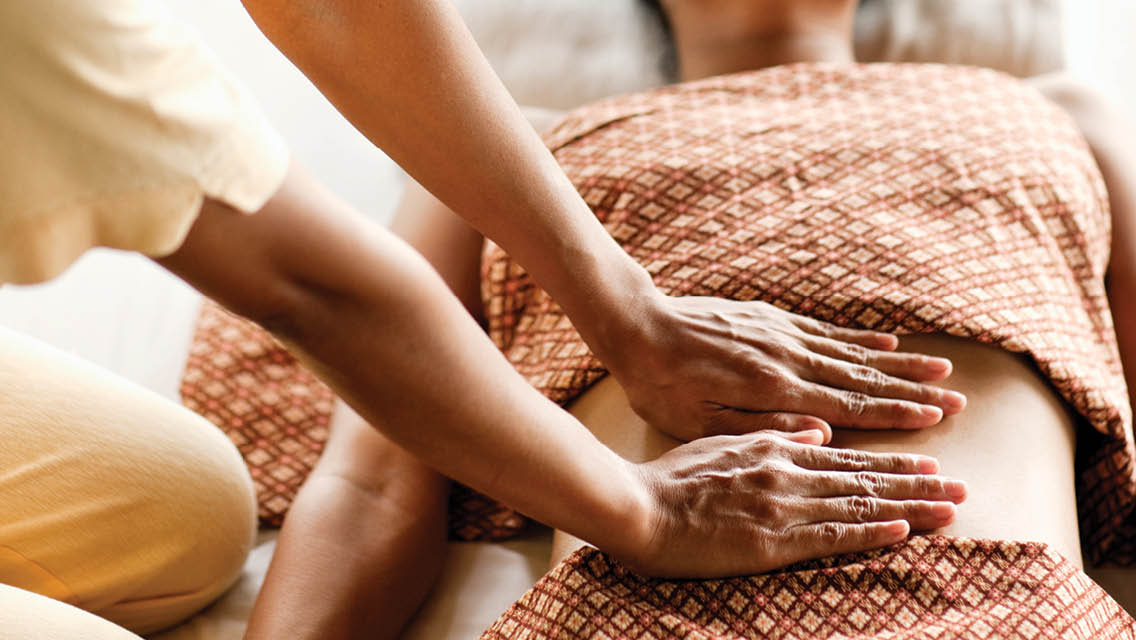 a massage therapist places her hands on a client's stomach