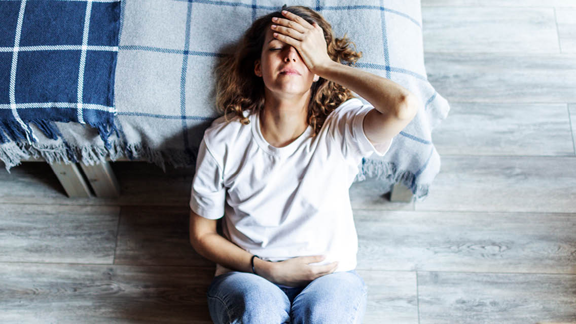 a woman sits on the floor holding her head and stomach