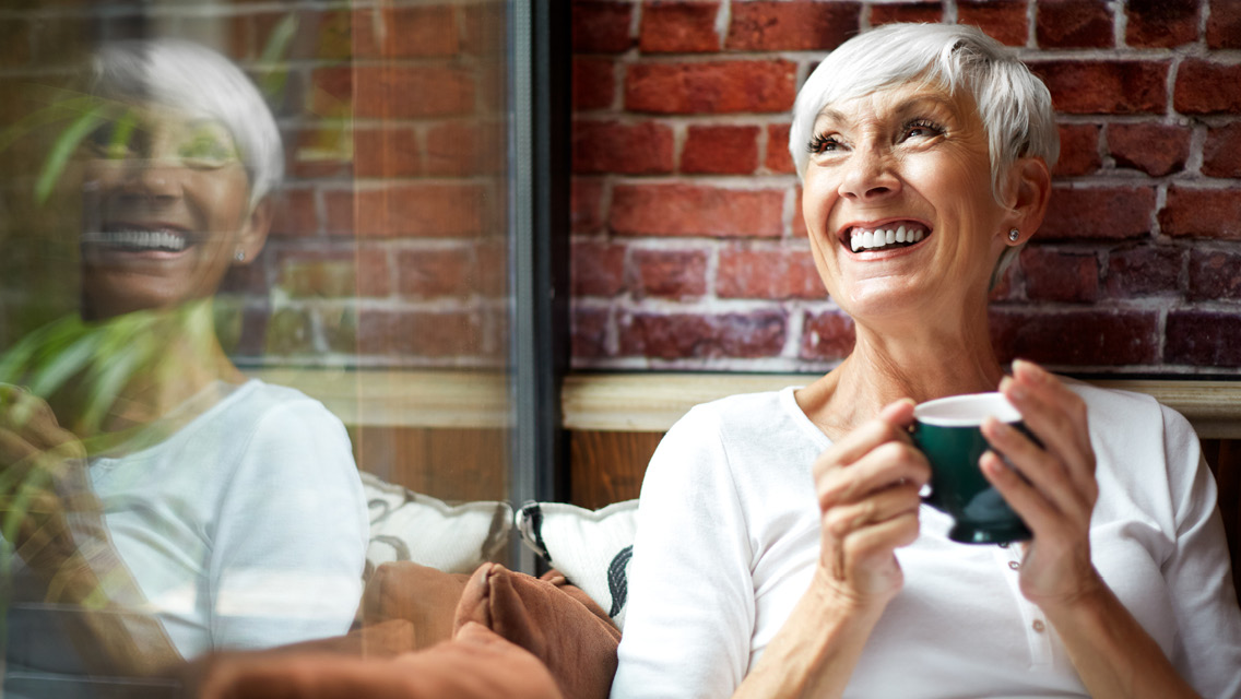 a woman with silver hair smiles while drinking a cup of tea