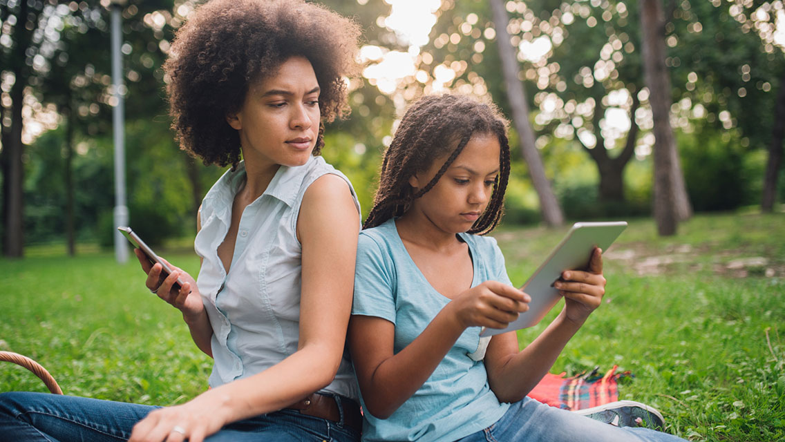 A mother and daughter are both on devices.