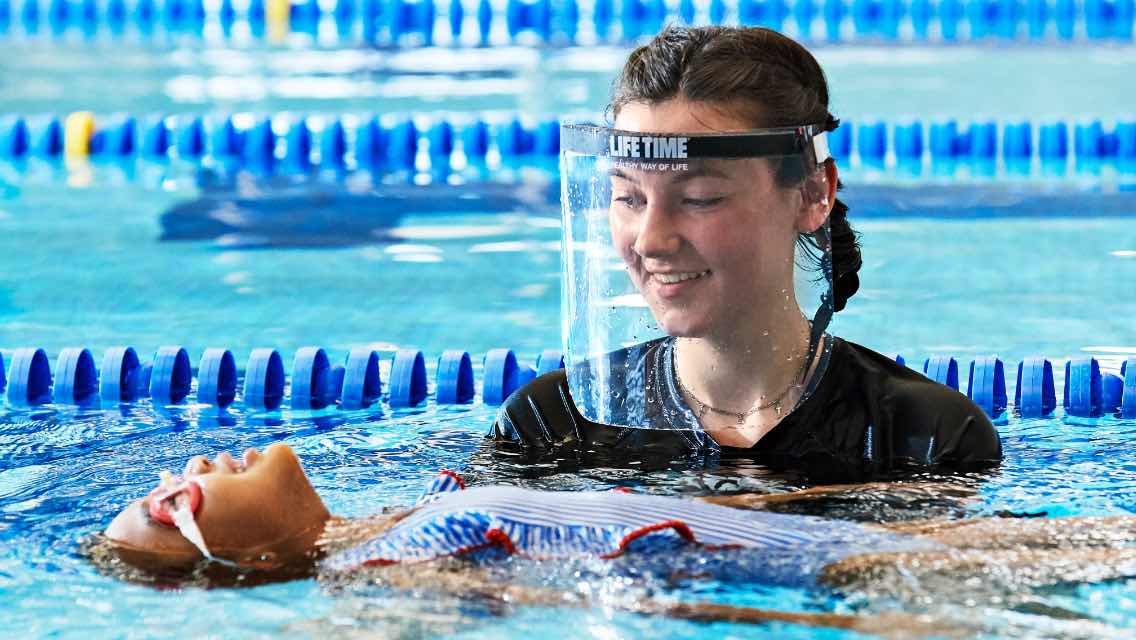 a Life Time swim instructor helps a child float on her back