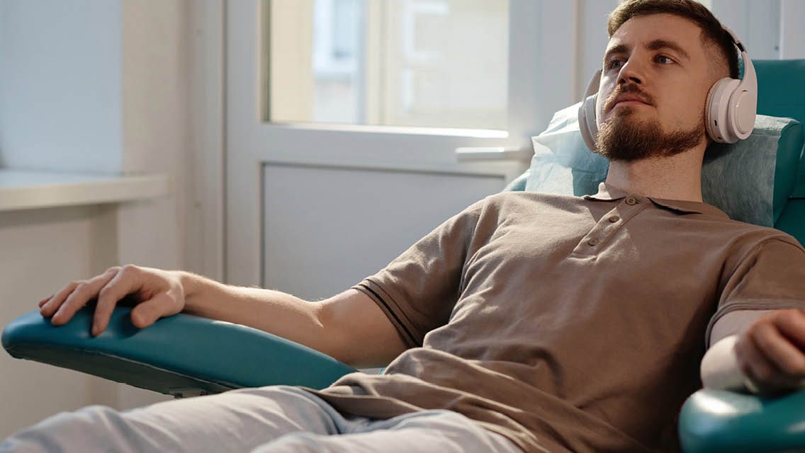 a man sits in a clinical sitting with headphones on receiving ketamine