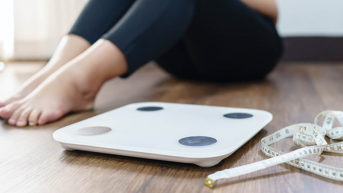 a woman sits next to a scale and measure tape